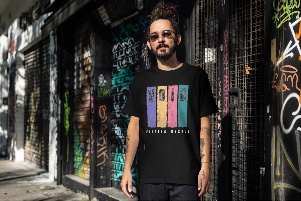 Man wearing a black t-shirt with colorful text standing in front of a graffiti-covered wall.