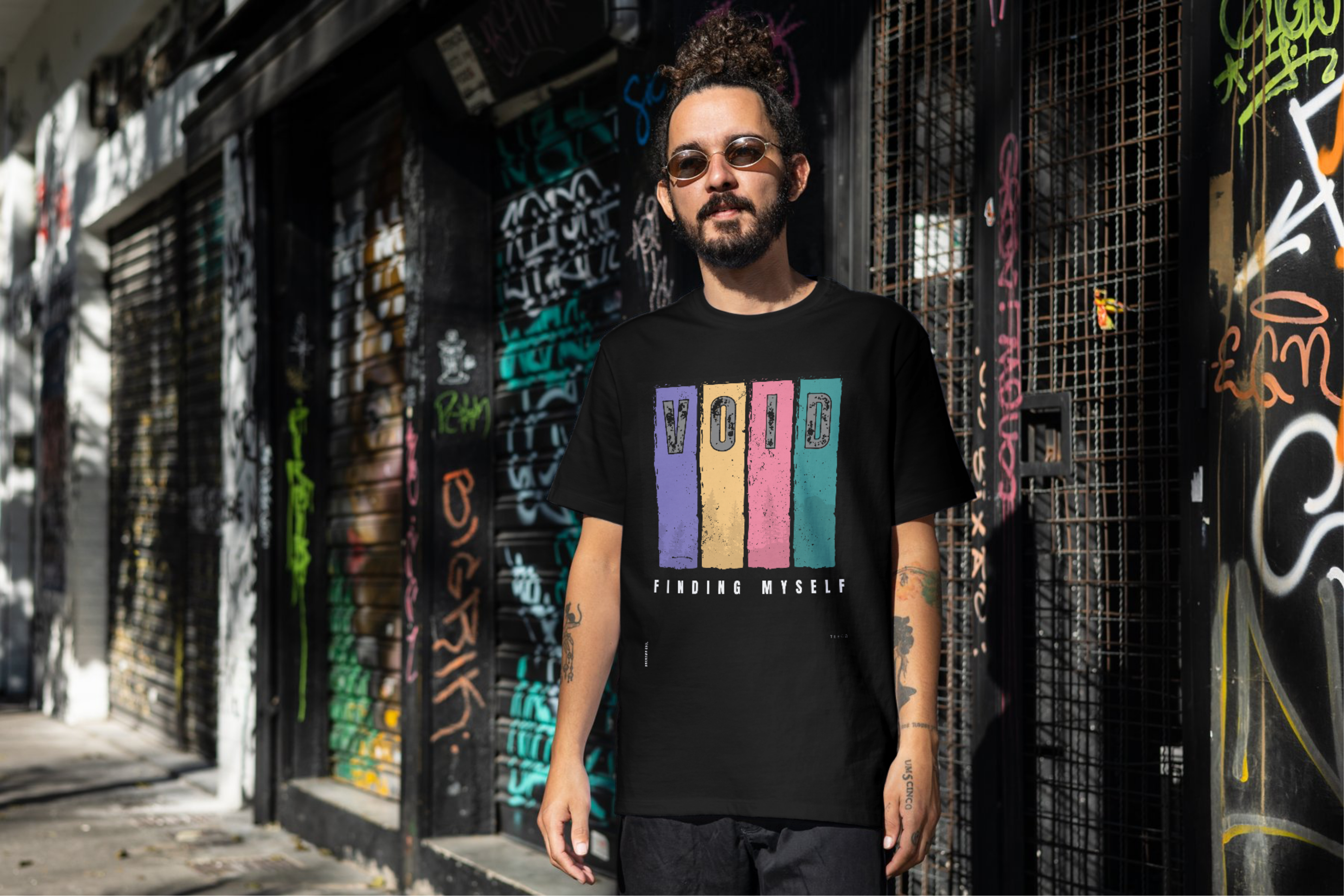 Man wearing a black t-shirt with colorful text standing in front of a graffiti-covered wall.